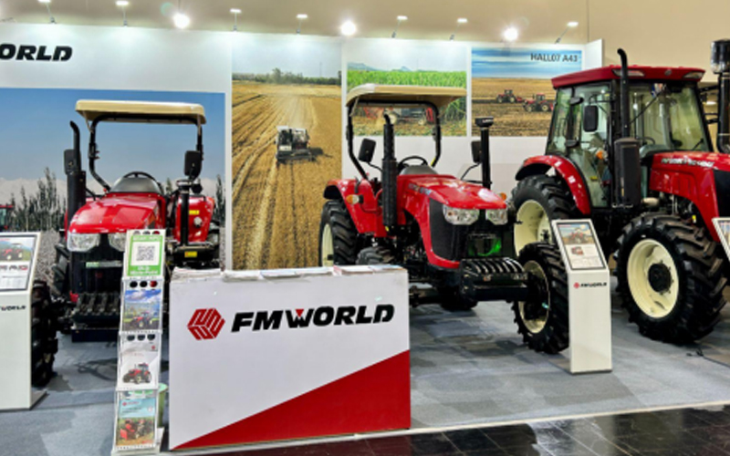 Agricultural expo booth featuring three tractors—compact, medium, and large sizes—amidst farmland scenery, with prominent ‘FMWORLD’ branding.