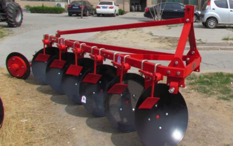 A red disc plow with multiple discs is parked in a paved area