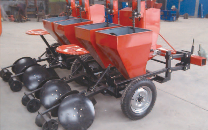 A red four-row planter with seed hoppers, furrow openers, and covering discs.