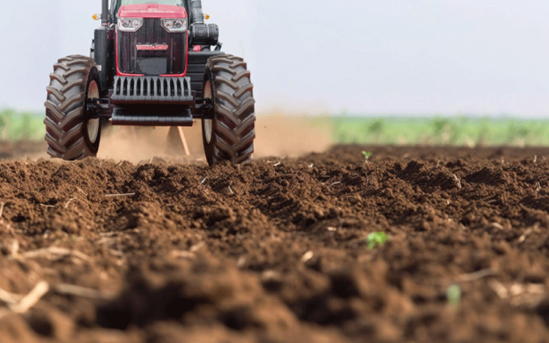 Low-angle photo of a red tractor with a black front and large grille plowing a field.