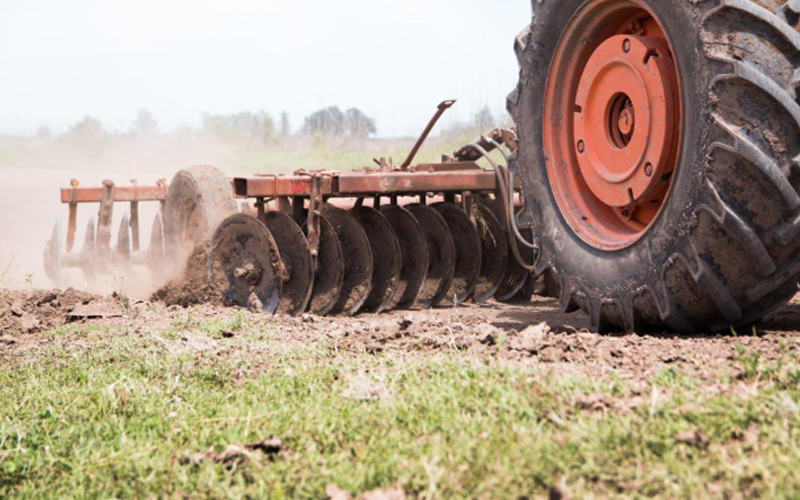 Big tractor equipped with heavily treaded tires engaged in land cultivation.