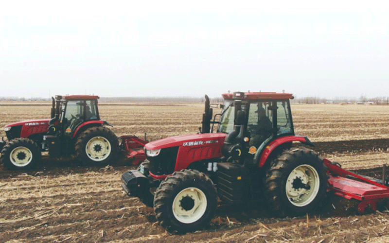 Two red FMWorld tractors are plowing in the field.