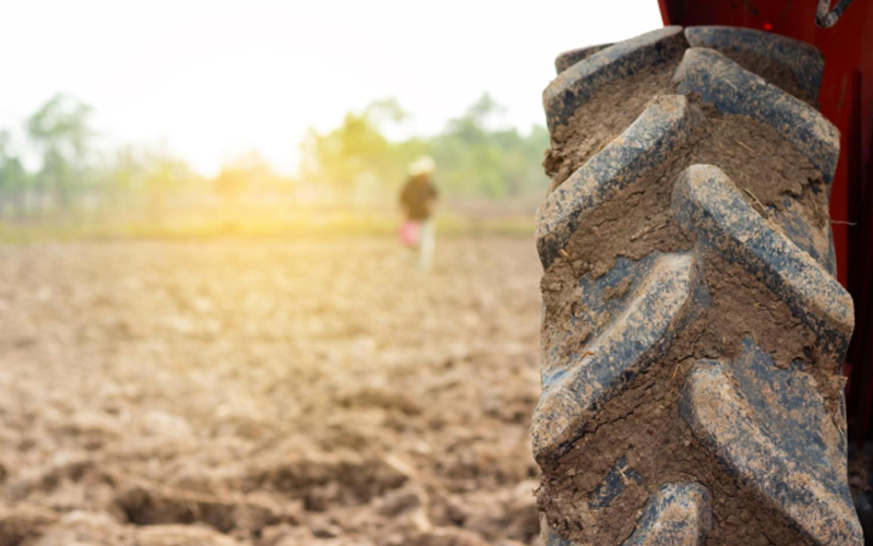 A muddy tractor with large tires plowing through a fertile field, preparing the soil for planting.