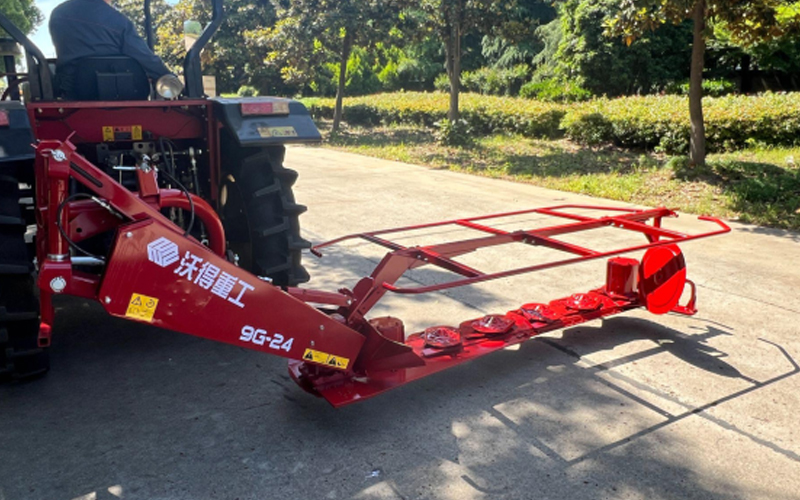 A red tractor with a World 9G-24 mounted mower attachment is parked on a paved surface.